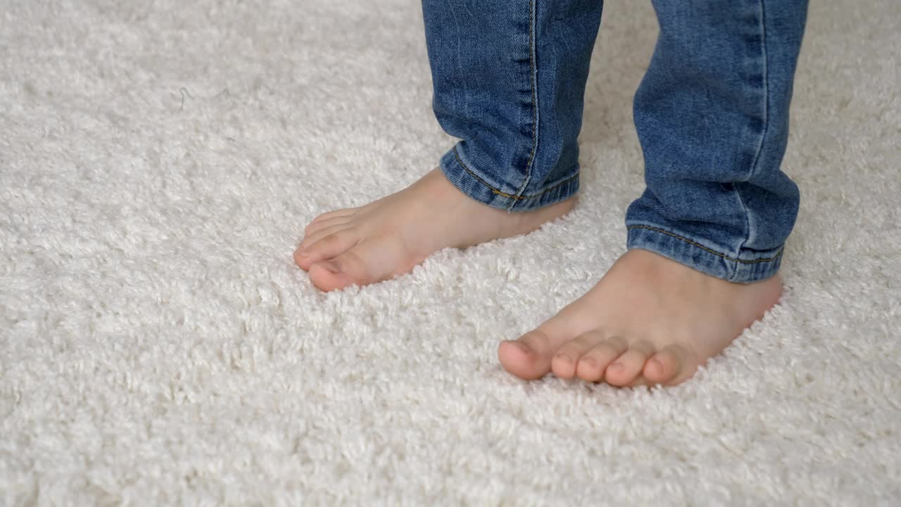 穿着牛仔裤的赤脚小男孩走在柔软的白色地毯上视频下载