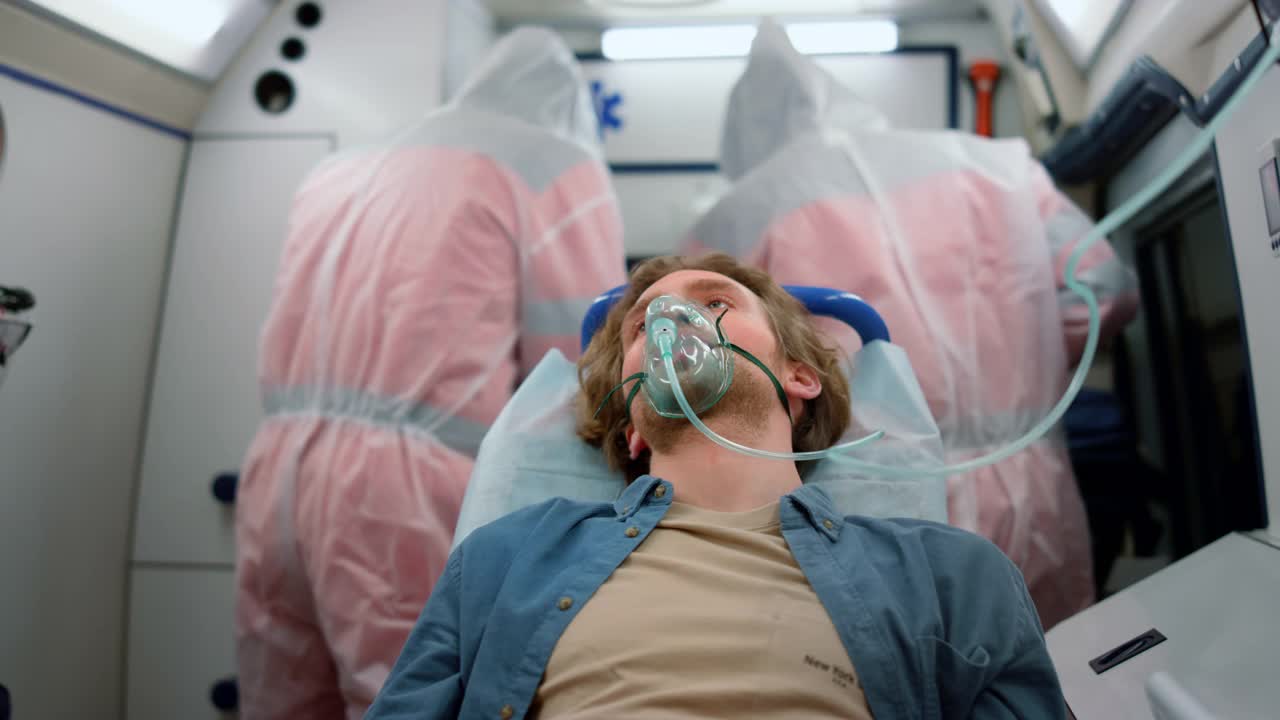 一名男子坐在救护车的担架上。受害者戴着氧气面罩呼吸视频素材