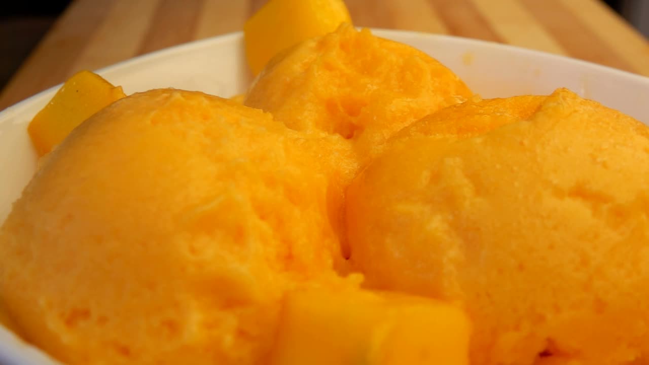 新鲜的芒果块落在装满冰冻芒果冰淇淋的白色碗里视频下载