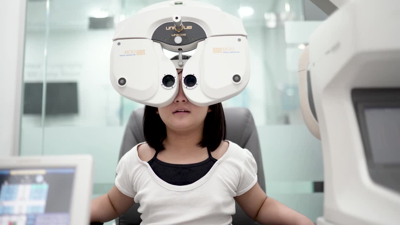 在眼科诊所，亚洲华人女孩坐在椅子上用数码相机做视力测试视频下载