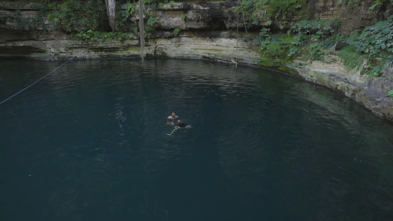 一对微笑的夫妇在天然井中游泳和玩耍的极端广角镜头视频下载