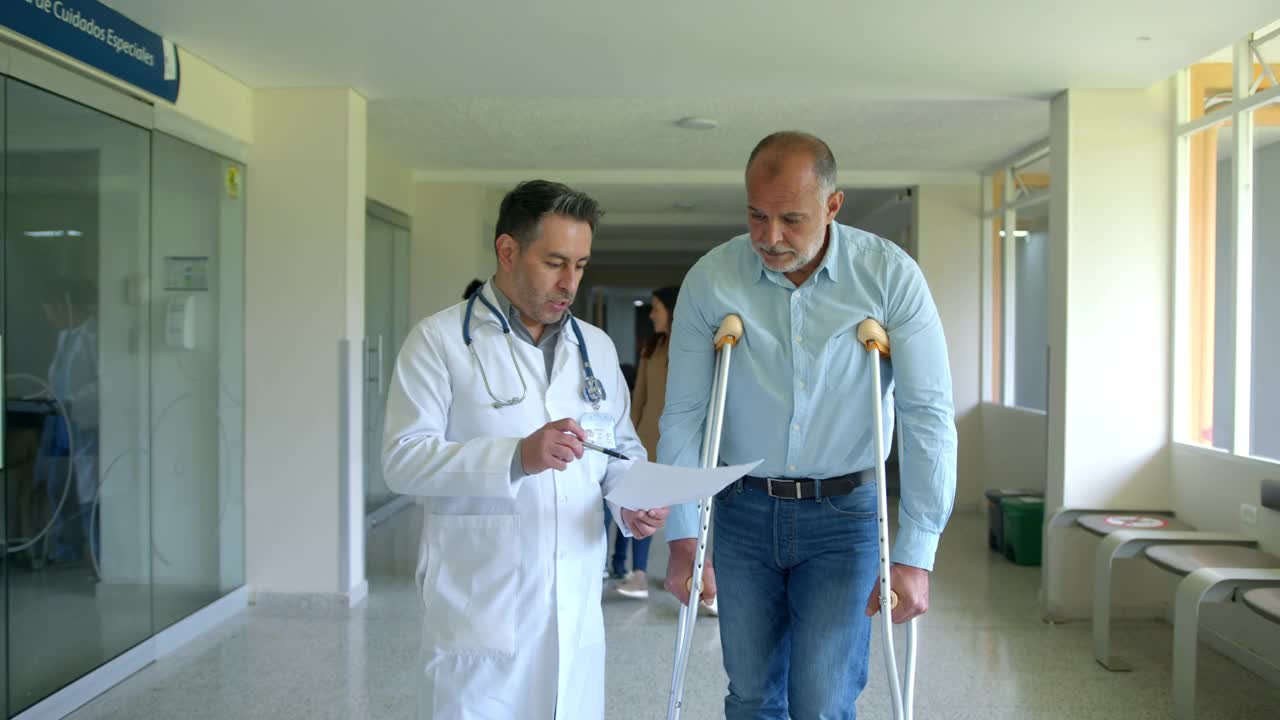 拄着拐杖的老年男性患者走在医院的整形外科医生旁边，看着医生讲解处方视频素材