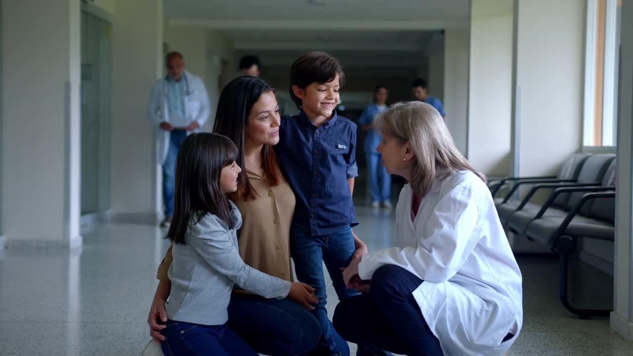 快乐的拉丁美洲资深女医生在医院走廊与带着孩子的单身母亲交谈视频素材