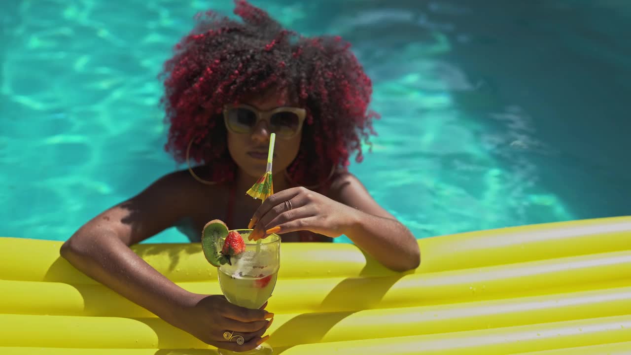 年轻女子漂浮在游泳池里，喝着热带鸡尾酒视频下载