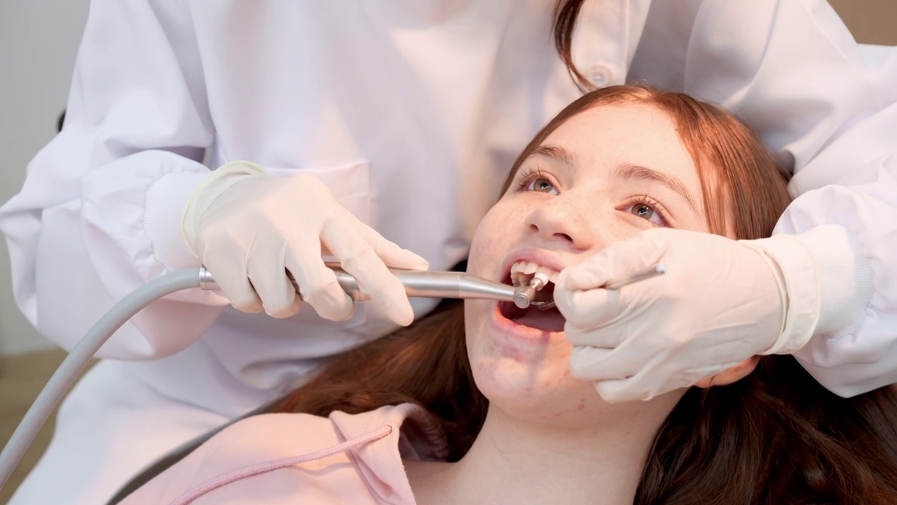 特写:十几岁的小女孩坐在牙科病房，张开嘴，让牙科医生用斜镜、吸唾液等牙科设备检查和清洁牙齿视频素材