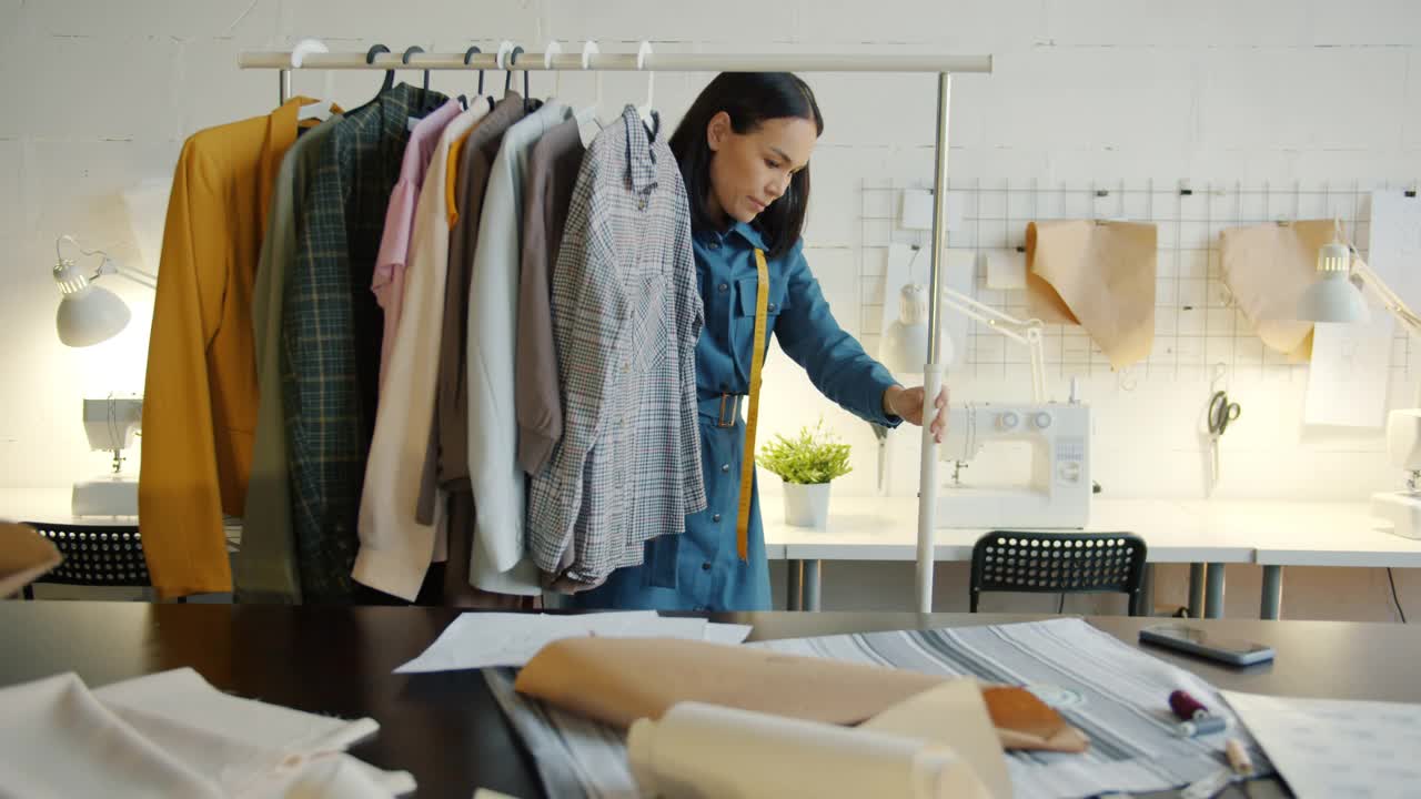 慢动作的年轻裁缝移动轨道与新衣服在现代工作室视频下载