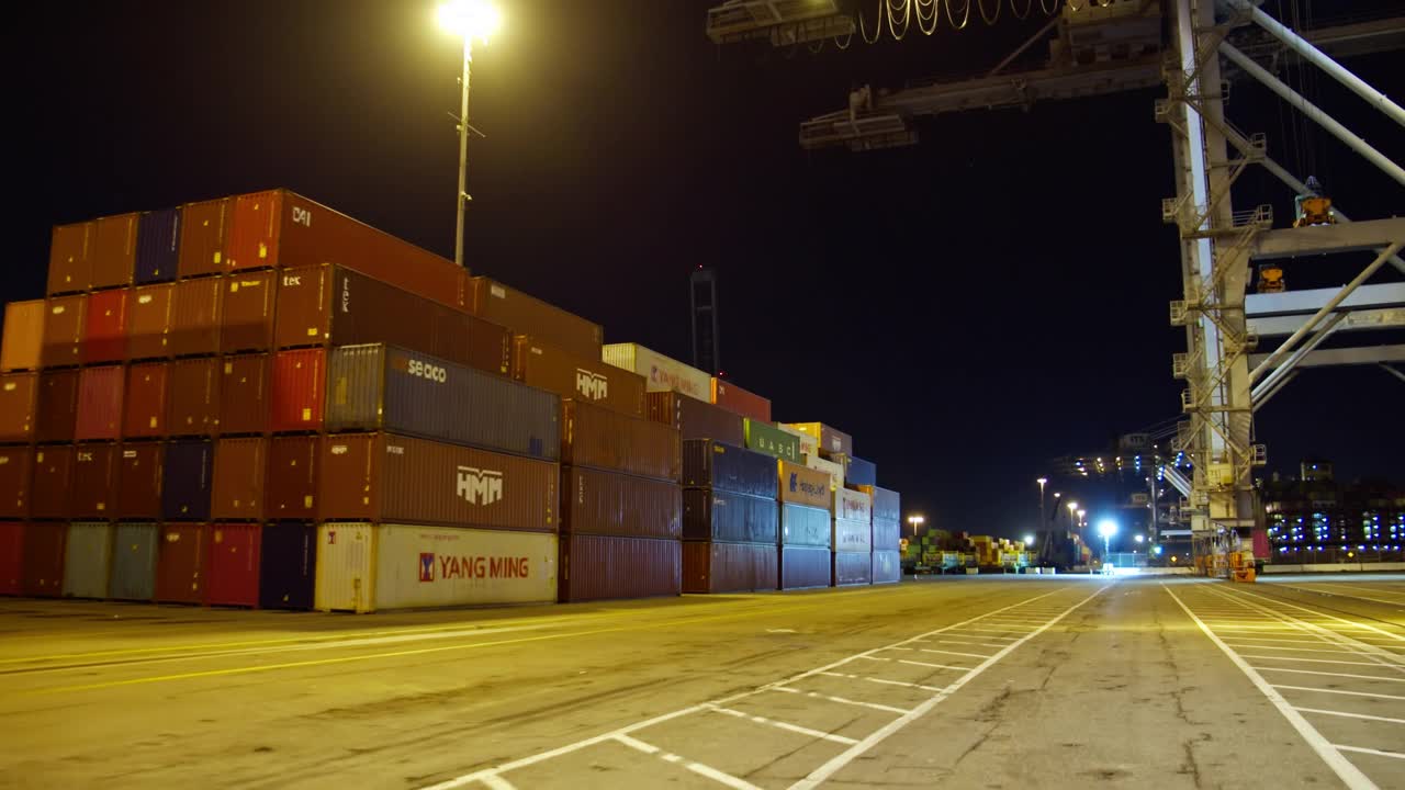 在航运码头，夜间缓慢驶过灯火通明的集装箱堆视频下载