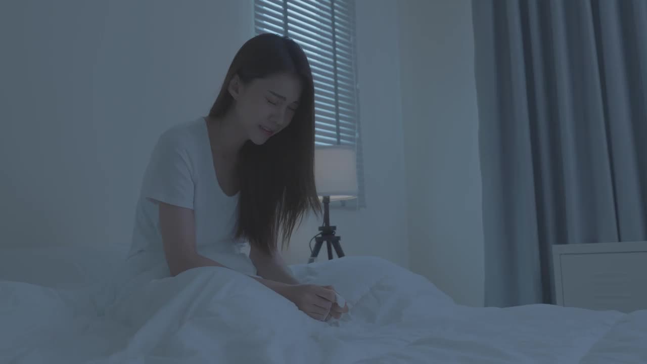 穿着睡衣的亚洲生病女孩在床上打喷嚏。有吸引力的年轻女子感觉不好，遭受过敏，把纸巾盖住她的鼻子，而在睡觉时打喷嚏在房子。视频素材
