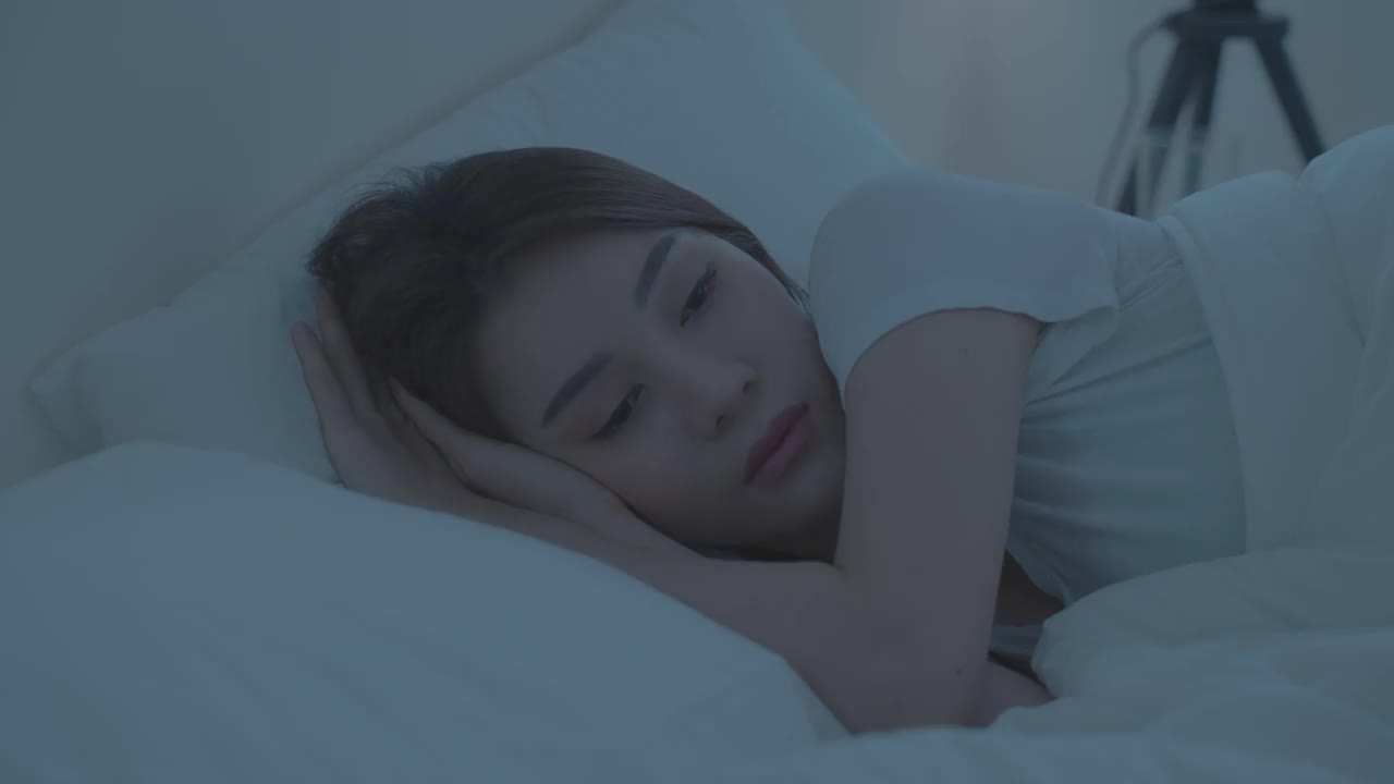 亚洲美丽的悲伤沮丧的女孩独自躺在床上的卧室。有吸引力的不快乐的年轻女子感到孤独和沮丧的压力，面对和思考生活问题在黑暗的夜房在家里。视频素材