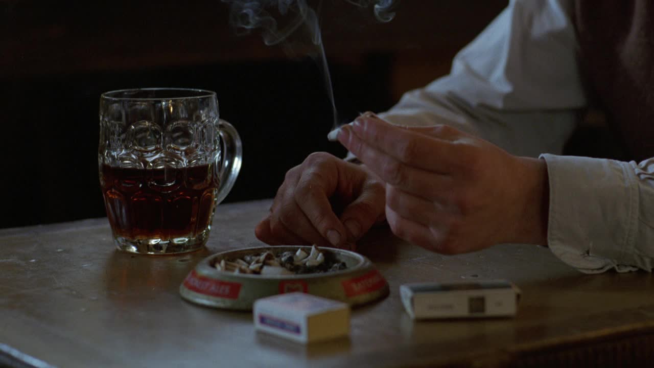 烟灰缸、啤酒杯、火柴盒和手握点燃的香烟的亲密角度。烟。视频下载