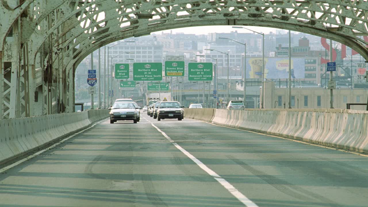昆斯伯勒大桥上汽车驶向摄像机的广角镜头。绿色高速公路标志和多层建筑皇后，长岛可见在bg。土星sl2汽车或轿车打滑和突然停止引起交通堵塞。汽车开始四处行驶视频下载