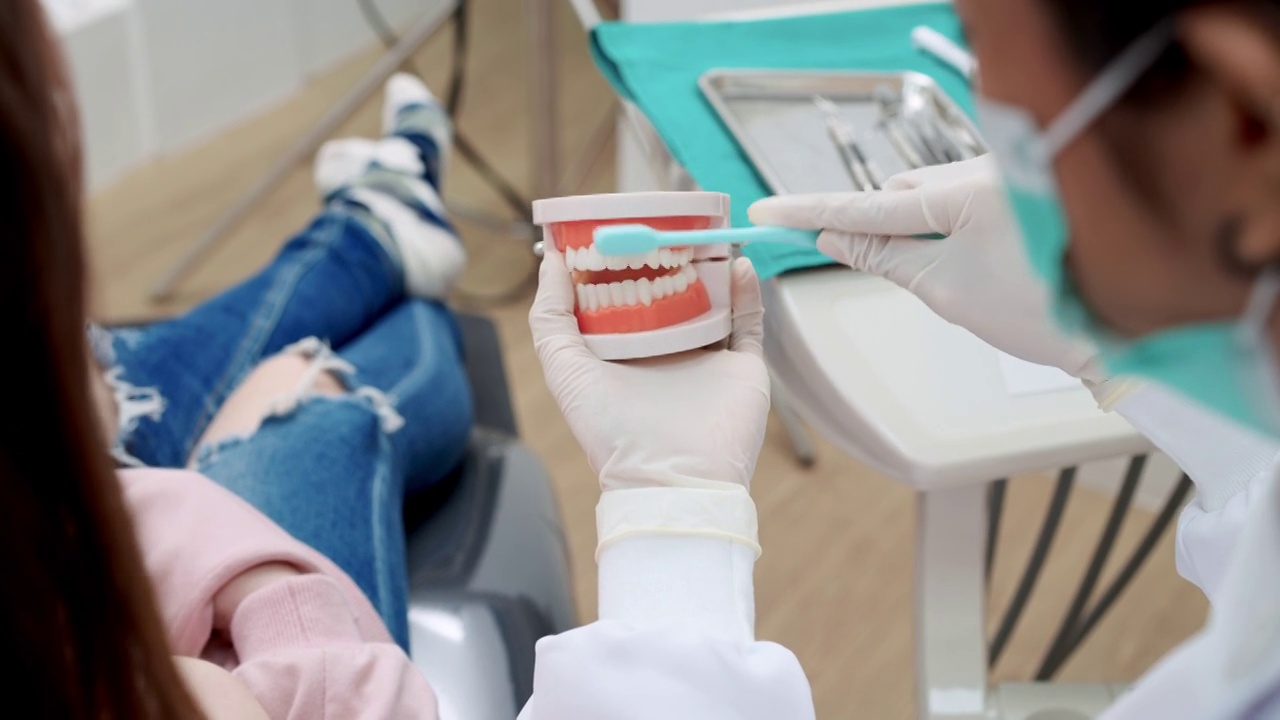 近距离观察:牙医向坐在牙科椅上的十几岁女孩展示如何正确刷牙，使用口腔和牙齿模型视频素材