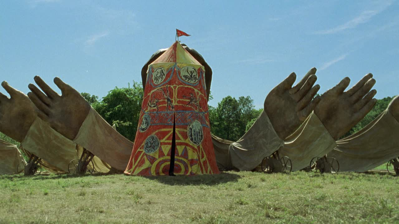 中角高马戏团帐篷在野外。巨大的纸模塑手雕塑围绕着帐篷。置于手推车或车轮上的手。森林和树木在bg。可能是嘉年华，马戏团，或者集市。蓝天白云。视频素材