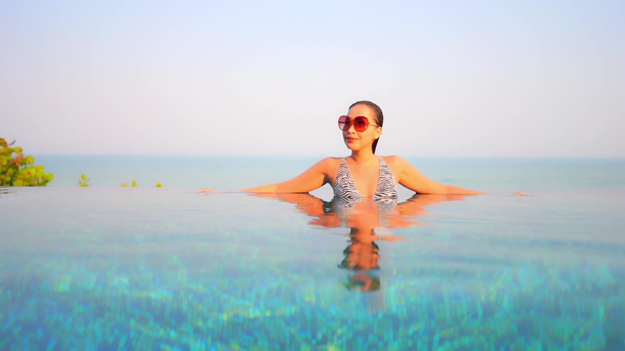 年轻的亚洲妇女放松愉快的户外游泳池视频下载