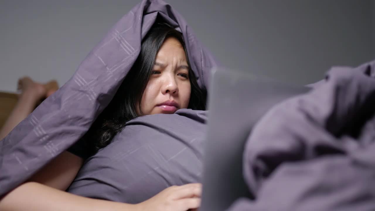 一位年轻女子在毛毯下看恐怖电影时感到害怕。视频下载