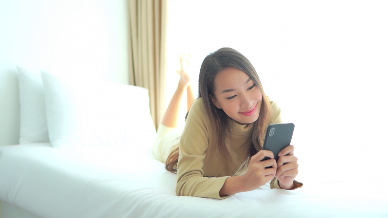 年轻的亚洲女性在床上使用智能手机视频素材
