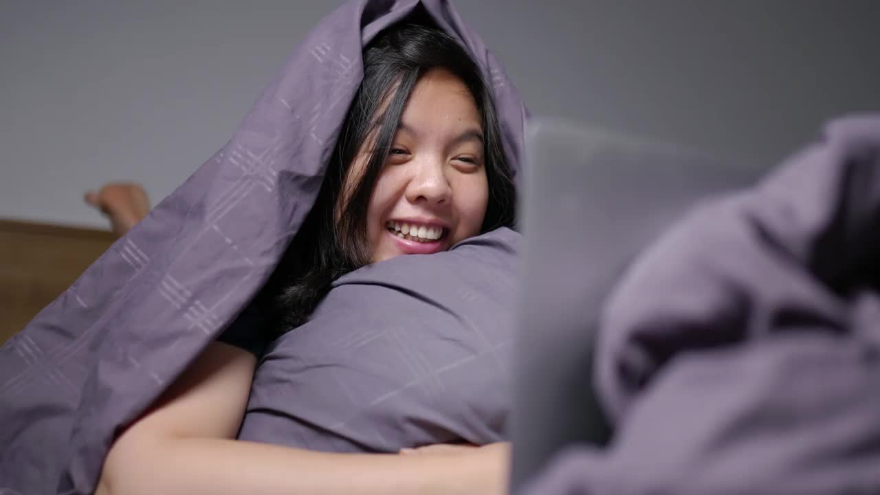 年轻女子盖着毯子看电影时开心地笑着。视频下载