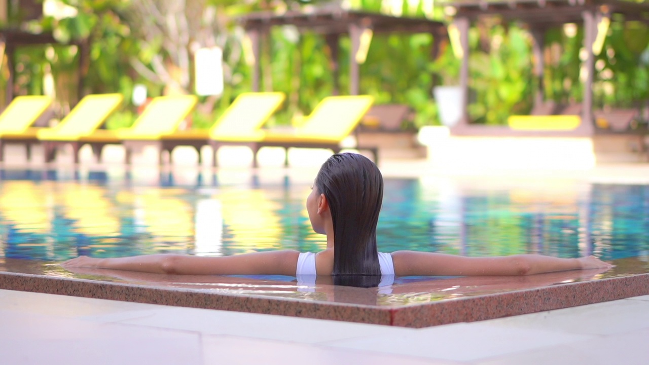 年轻的亚洲妇女放松愉快的户外游泳池视频下载