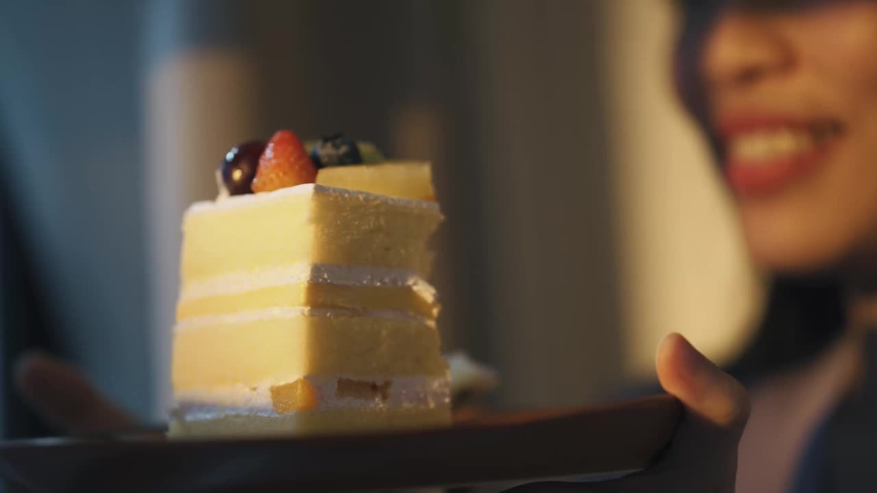 亚洲中国美女享受一片蛋糕在日落期间看着远方透过窗帘视频下载