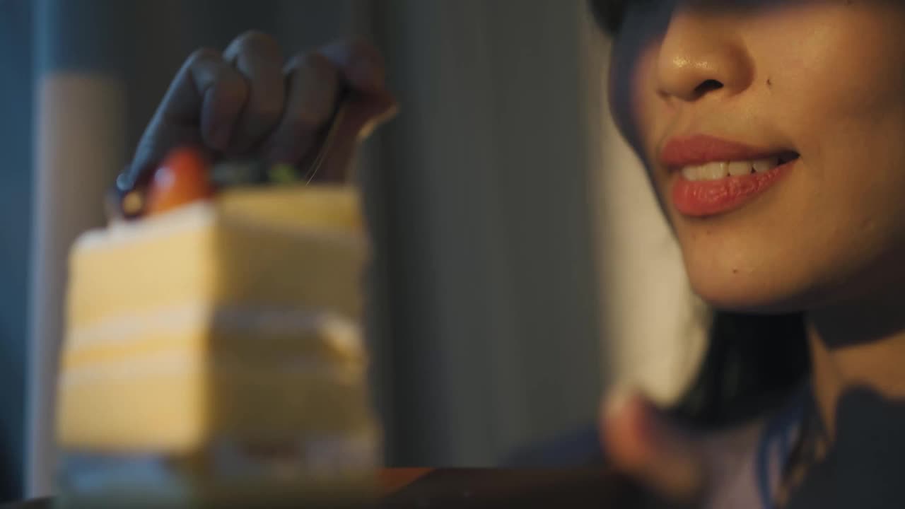亚洲中国美女享受一片蛋糕在日落期间看着远方透过窗帘视频下载