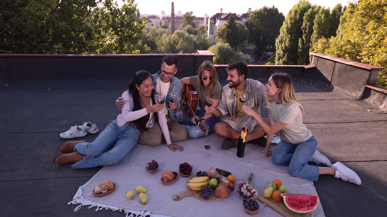 快乐的朋友们喝着葡萄酒，享受着吉他音乐在屋顶野餐。视频素材