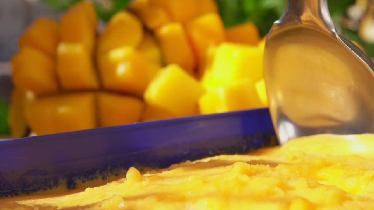 勺子正在舀冰冻芒果冰淇淋，以成熟的芒果为背景视频下载