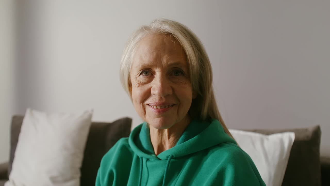 一位老妇人微笑着看着相机，坐在沙发上，特写视频素材