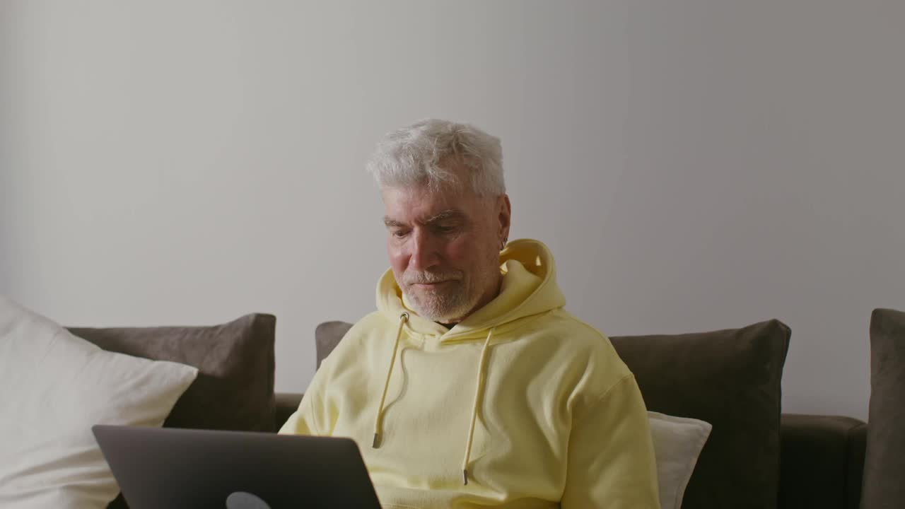 一位上了年纪的男子微笑着看着相机，从笔记本电脑上抬起头来视频素材