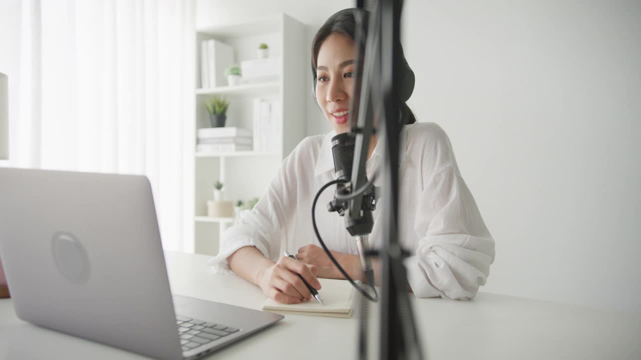 年轻的亚洲妇女在她的笔记本电脑从家庭工作室录制播客。视频下载