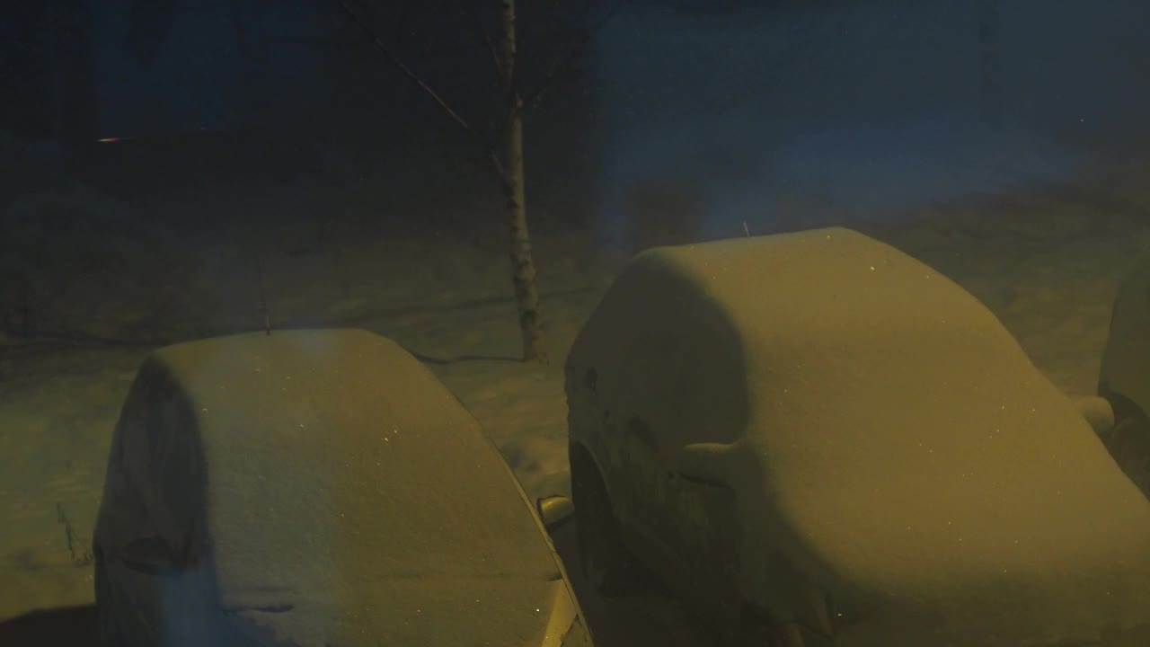 雪在院子里，在停车场里，一盏黄色的路灯照亮着。坏天气。汽车上到处都是雪视频素材