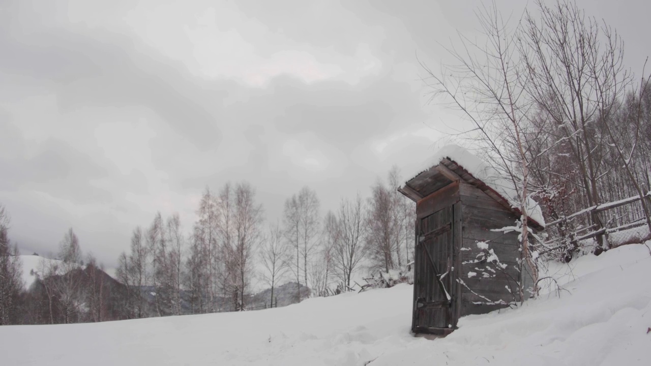 在一个寒冷的冬天，坐落在树叶繁茂的森林边缘的一间被雪覆盖的小木屋视频素材