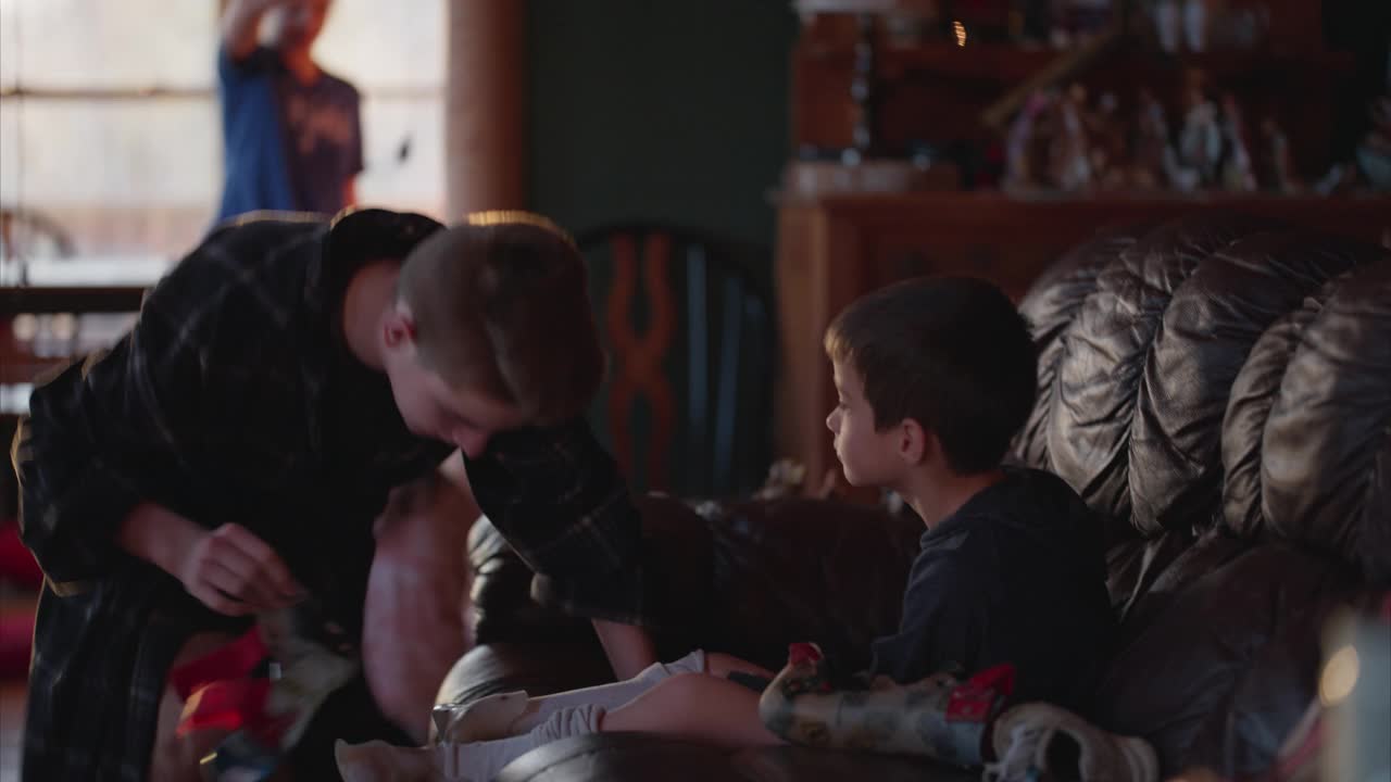 圣诞节早晨，一名少年帮助残疾男孩戴上腿部支架视频素材