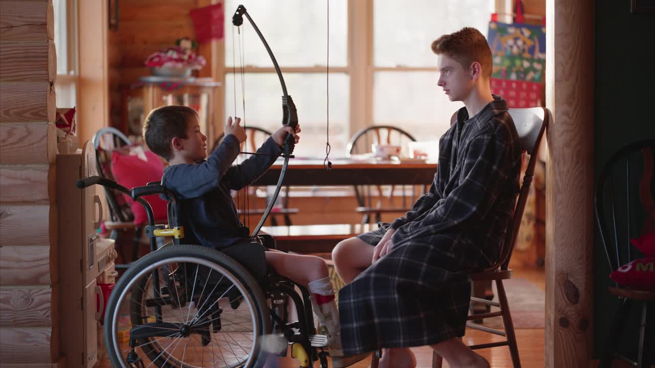 圣诞早晨，坐在轮椅上的小男孩在玩弓箭视频素材