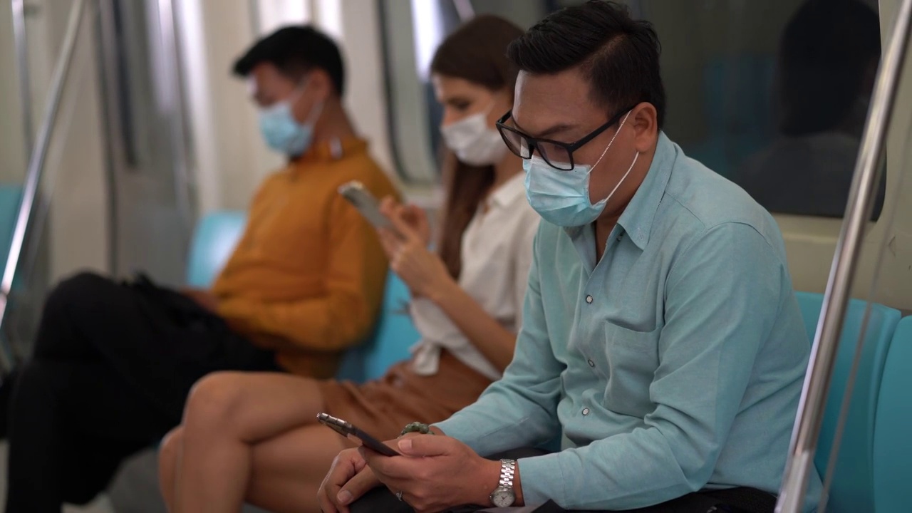 一群戴着外科口罩的人挤在一起，在地铁里听音乐。在冠状病毒或Covid-19大流行期间，公共交通是新常态视频下载