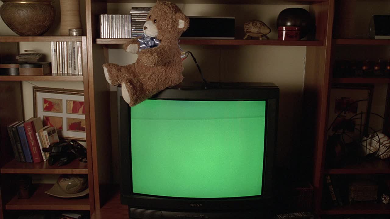 中等角度的泰迪熊坐在绿色屏幕的电视上，在家庭办公室或书房。BG的书架。泰迪熊可能是隐藏的保姆摄像机。视频下载