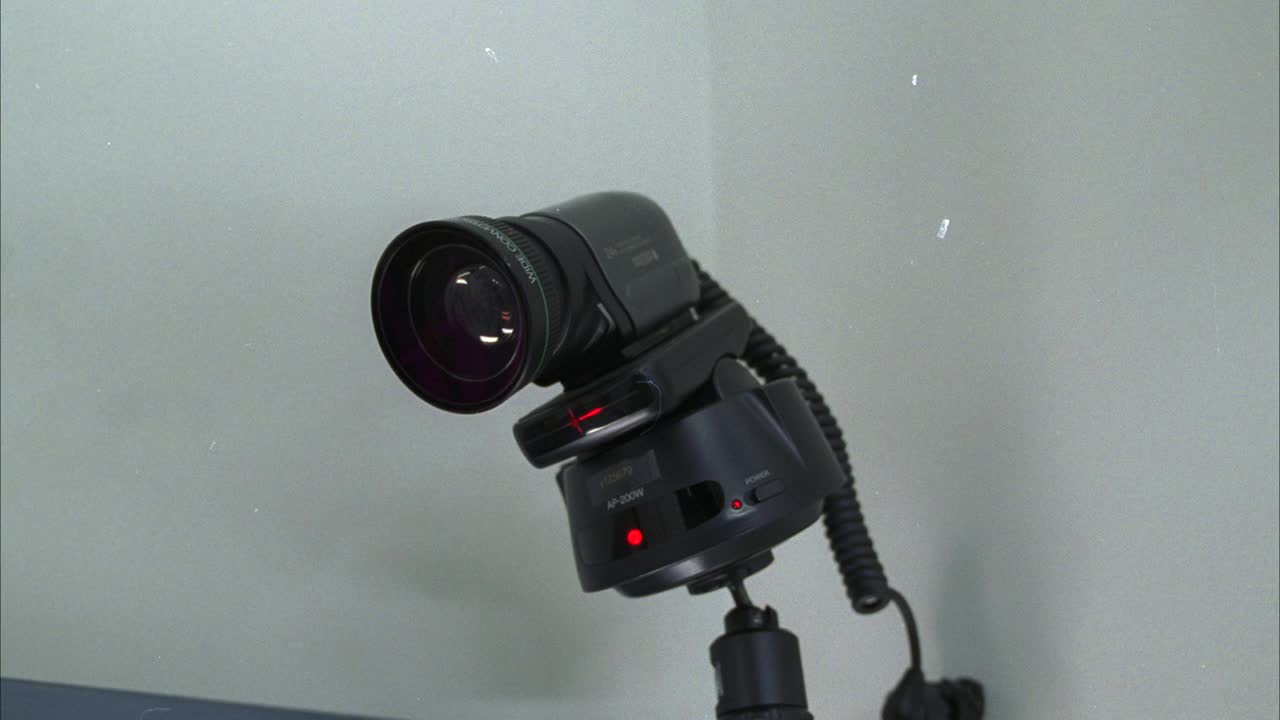 安装在墙上的安全摄像头的近角度。相机的镜头前后摇摄了好几次。相机上的红灯亮了。视频下载