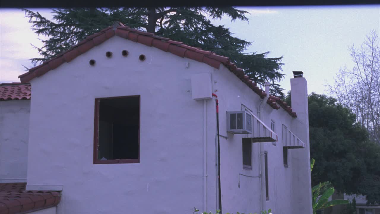 Pan从左到右的西班牙灰泥风格的房屋或住宅区的公寓建筑被树木包围。遮阳篷窗口。建筑物后面的电线和排水管。视频下载