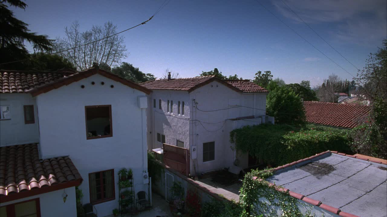 西班牙灰泥风格的公寓建筑、房屋或别墅的高角度下降。屋顶可见。绿树成荫，蓝天环绕的住宅区。电线悬挂在建筑物上方。可能是电话线或特技用的电线。视频下载