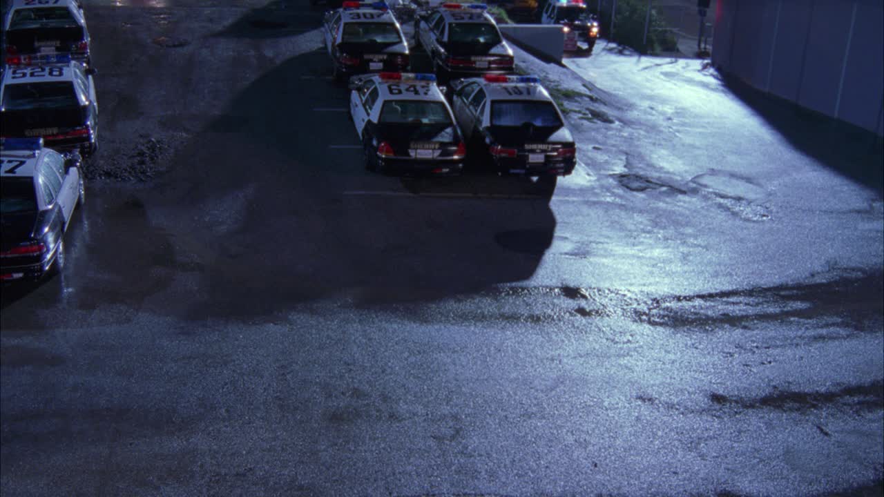 从高处俯拍停放着警车或警长的停车场。一辆警用suv带着闪光灯在停车场内行驶。可能是洛杉矶警局，洛杉矶警局。视频素材