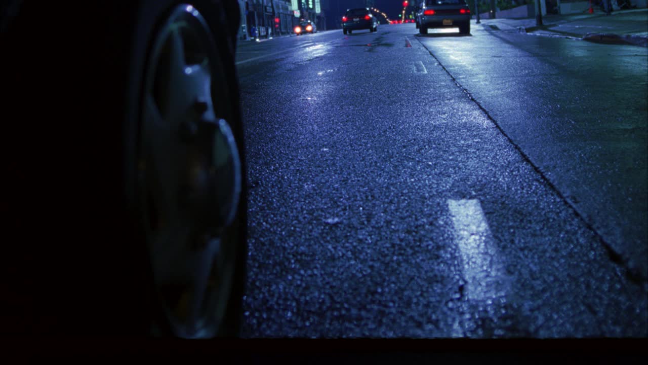 跟踪镜头近角度拍摄汽车或货车在城市街道超速行驶的轮胎或轮毂盖。轮胎在车流中穿梭。路面潮湿或下雨。尾灯。视频下载