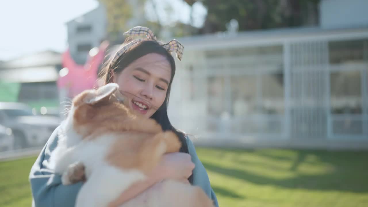 快乐在一起，有吸引力的亚洲女性年轻的成年女性喜欢与可爱的柯基狗玩，日落在室外草地后院视频下载