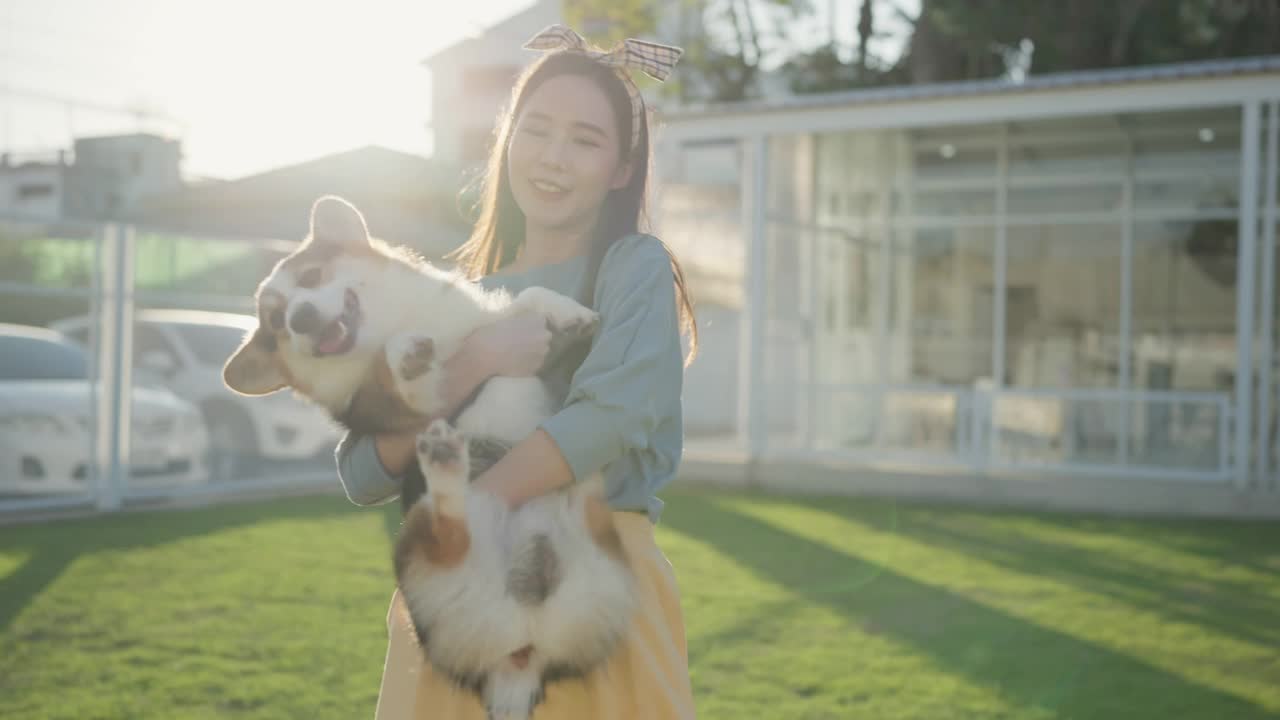快乐在一起，有吸引力的亚洲女性年轻的成年女性喜欢与可爱的柯基狗玩，日落在室外草地后院视频下载