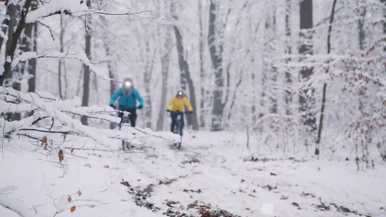 开着车灯的情侣骑着电动自行车在雪地里的森林小路上视频下载