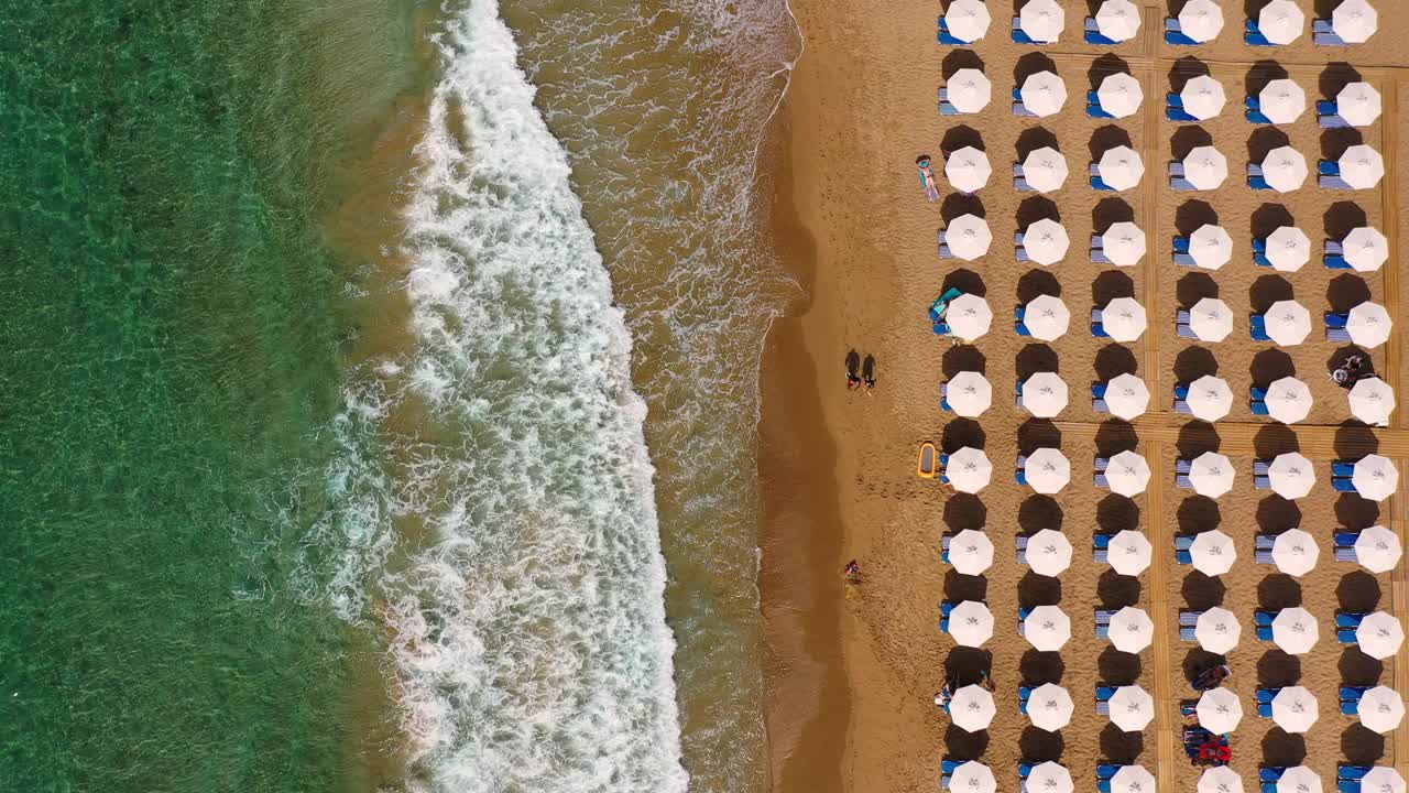 暑假的概念。从上面俯瞰，令人惊叹的航拍海滩，沙滩伞和蓝绿色清澈的海水。在沙滩上的伞下的太阳躺椅上的俯视图视频素材