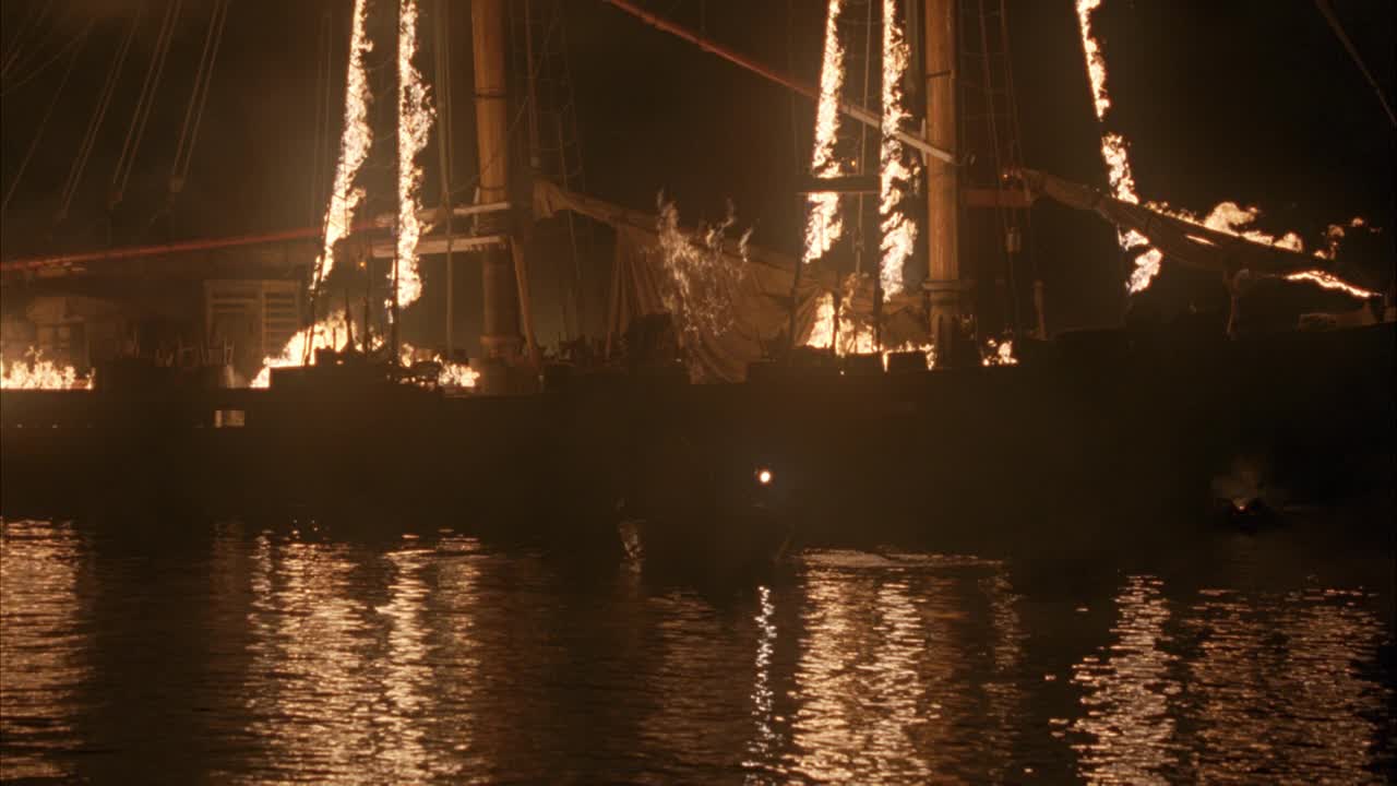 双桅船大角度着火。划艇上的人在平静的水面上向船外划去。船上deckÊ的人着火了，挥舞着手臂跳进水里。火焰在水中的反射。绳子。雾。帆船上。海洋。可能是海盗船。假话视频下载