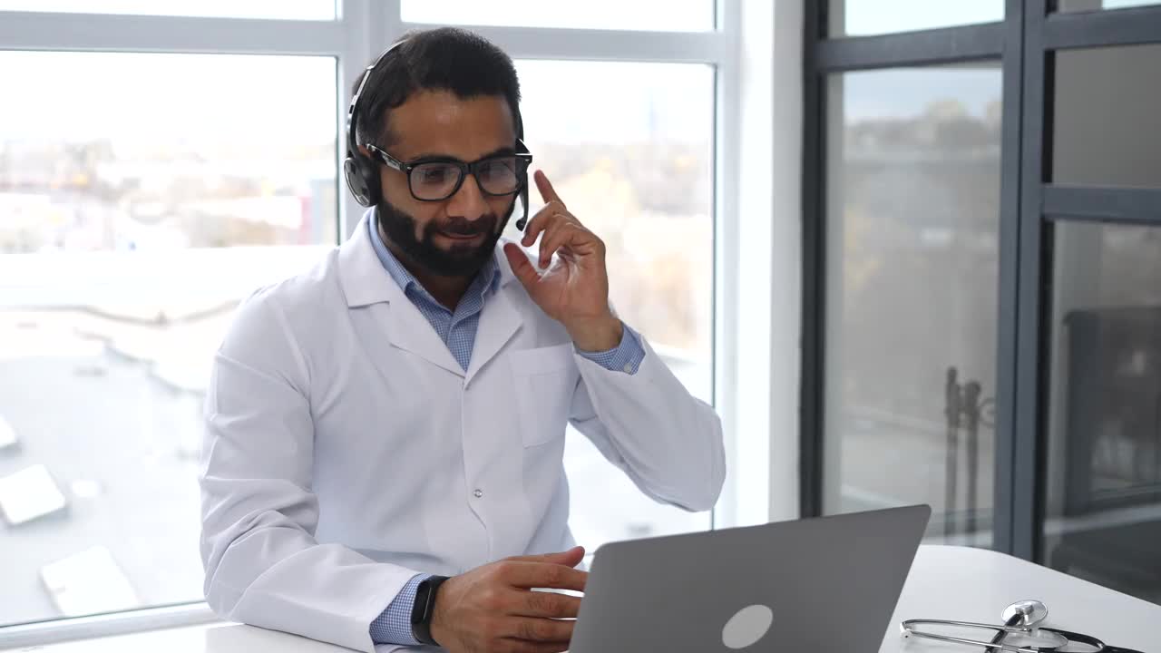 印度男性医学博士戴着耳麦、眼镜和病号服进行在线咨询视频素材