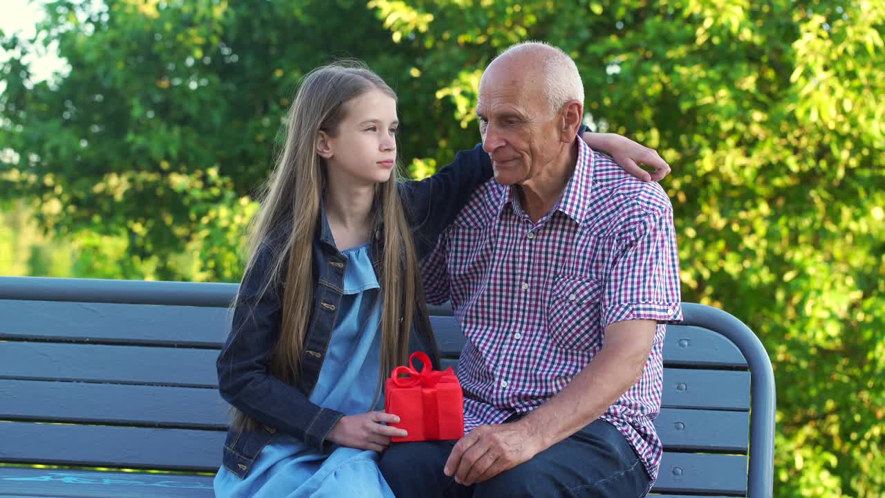 孙女把红色礼盒送给了坐在长椅上的老人视频下载
