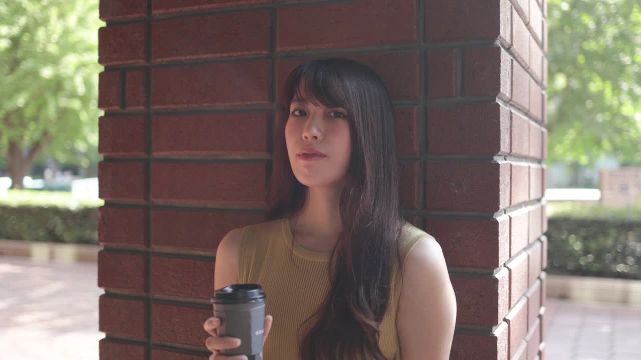 穿着黄色连衣裙的美丽女人靠在红色砖墙上，拿着一杯咖啡-第三部分的第二部分视频下载