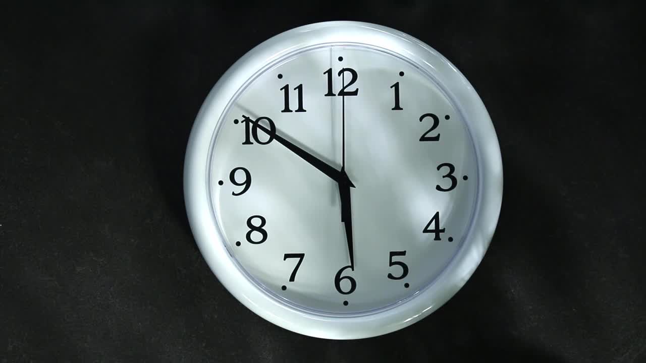 白色时钟在黑色的背景。秒针指向6点钟。晚上或早晨。视频素材