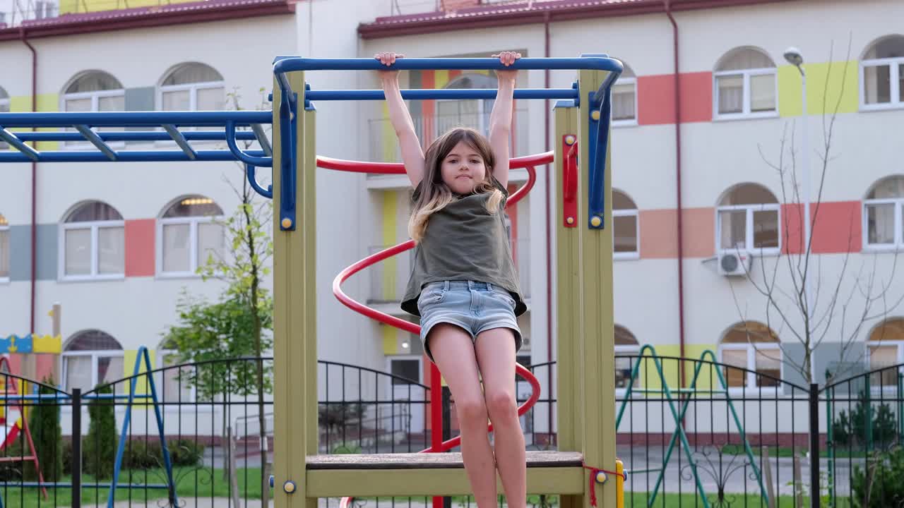 小女孩挂在运动单杠上。孩子在操场上玩耍视频素材